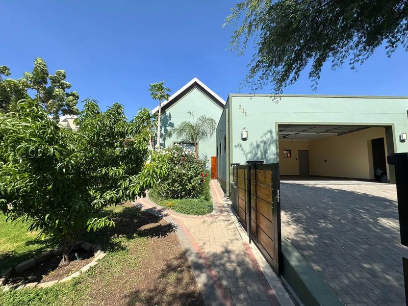 Front view of the property featuring a paved driveway, double garage, and a landscaped garden with a brick walkway leading to the entrance.