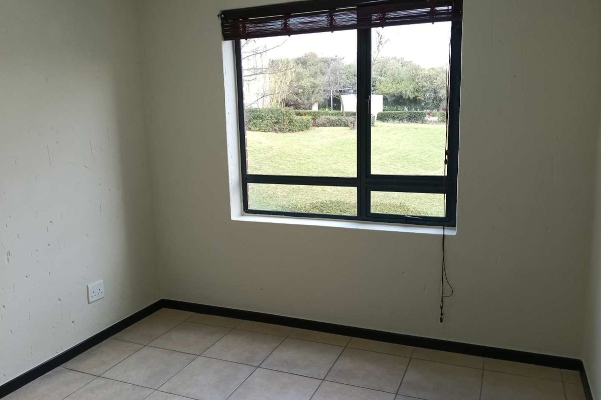 An empty bedroom featuring tiled flooring, an aluminium window frame with a blind, and views of the garden area.