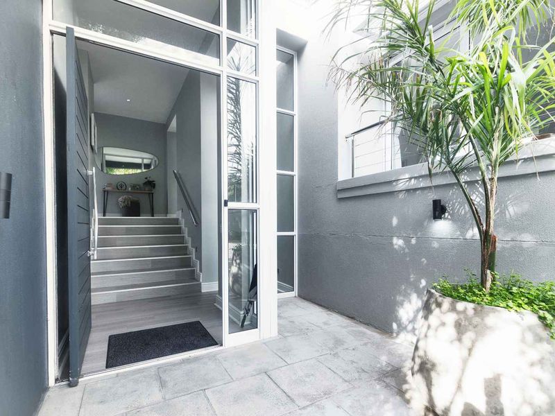 Modern entrance area featuring a large glass door, stone tiled flooring, and a staircase leading into the home interior.