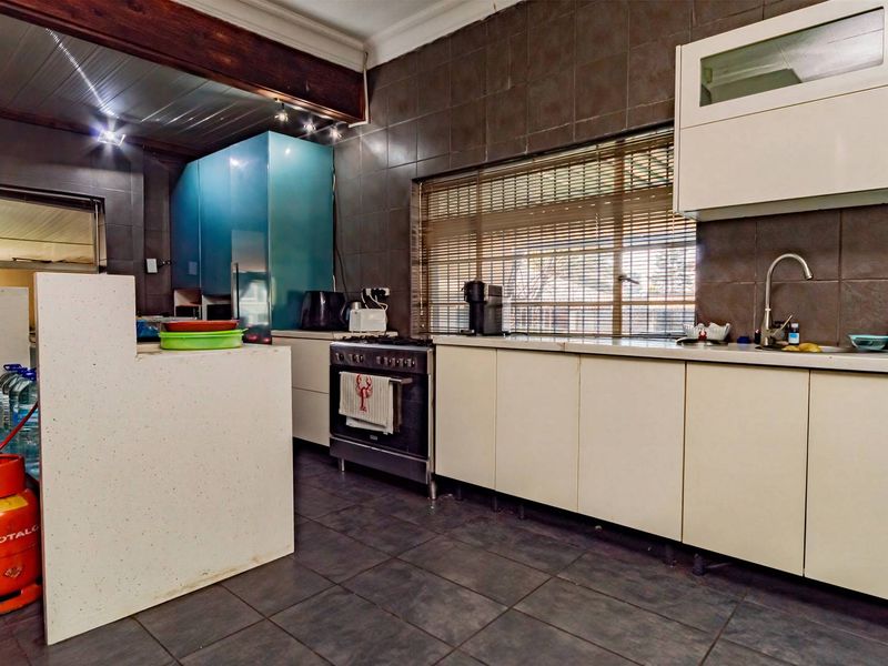 A functional kitchen featuring dark tiled walls and flooring, white cabinetry, a gas stove, and a timber ceiling.