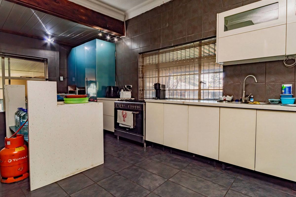 A functional kitchen featuring dark tiled walls and flooring, white cabinetry, a gas stove, and a timber ceiling.