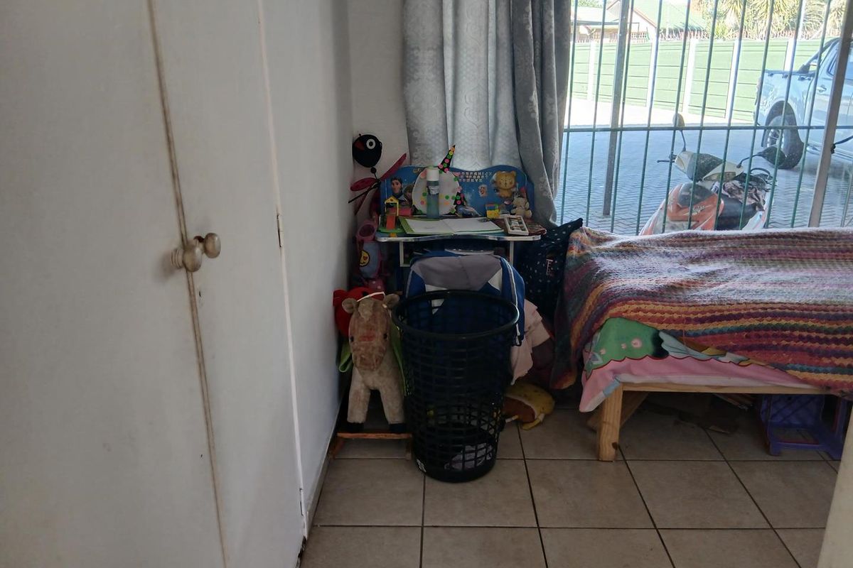 A bedroom featuring tiled flooring, a built-in cupboard, and security bars on the window.