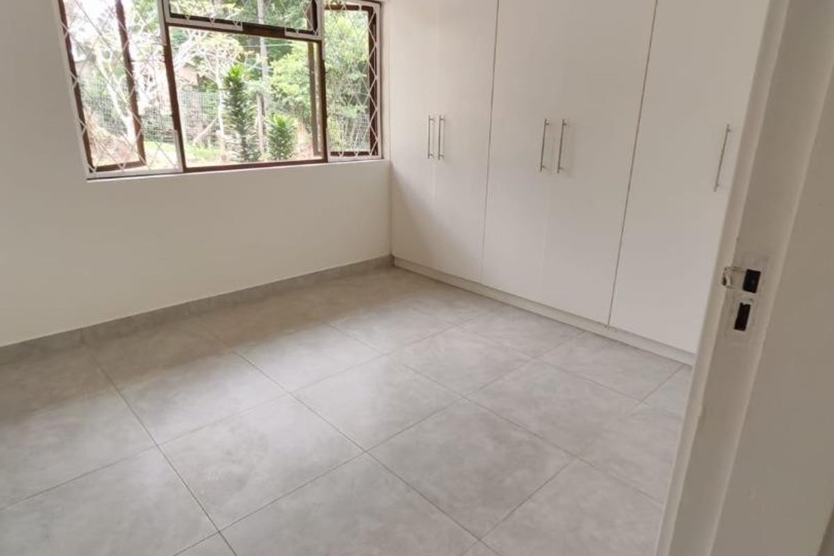 A bright, empty bedroom featuring neutral tiled flooring and extensive built-in white cabinetry, offering a clean and versatile space.