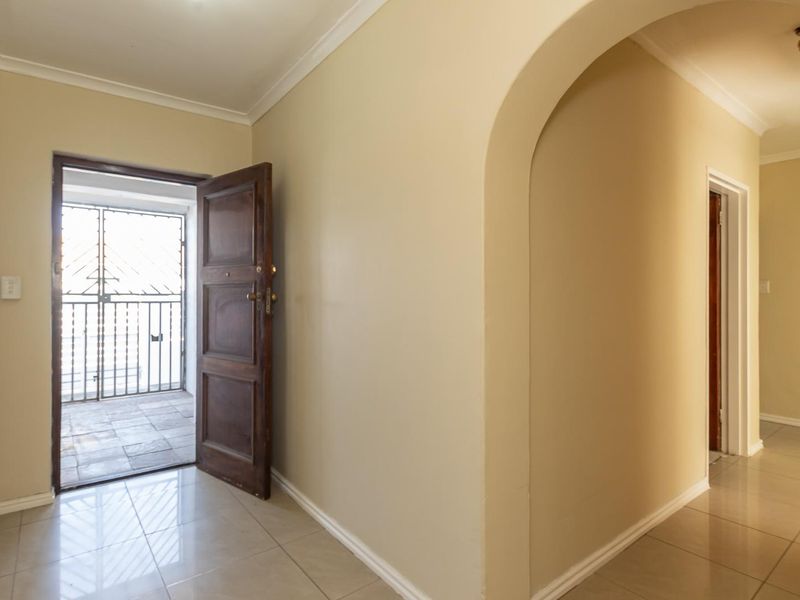 A bright and spacious entrance hall featuring tiled flooring, a decorative archway, and a solid wood door leading to a secure exterior area.