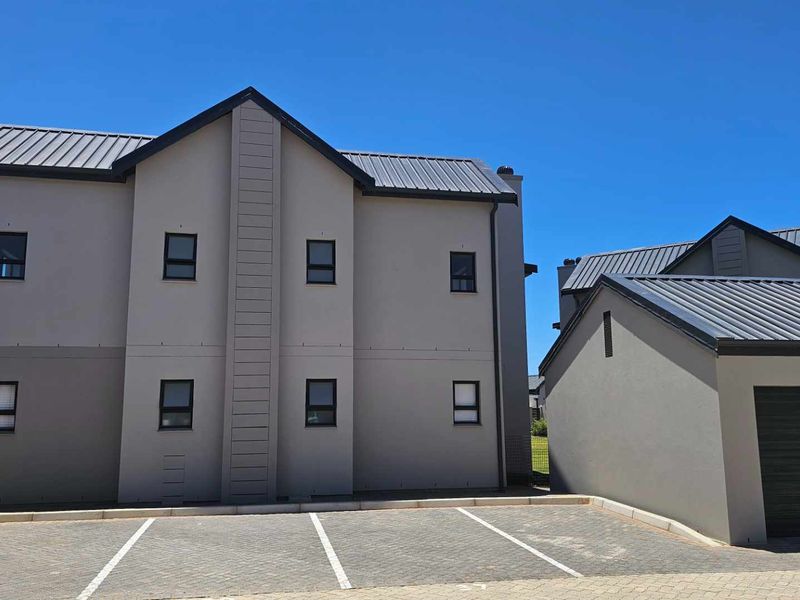 Modern apartment building exterior featuring a clean grey facade, metal roofing, and a paved driveway with an integrated garage.
