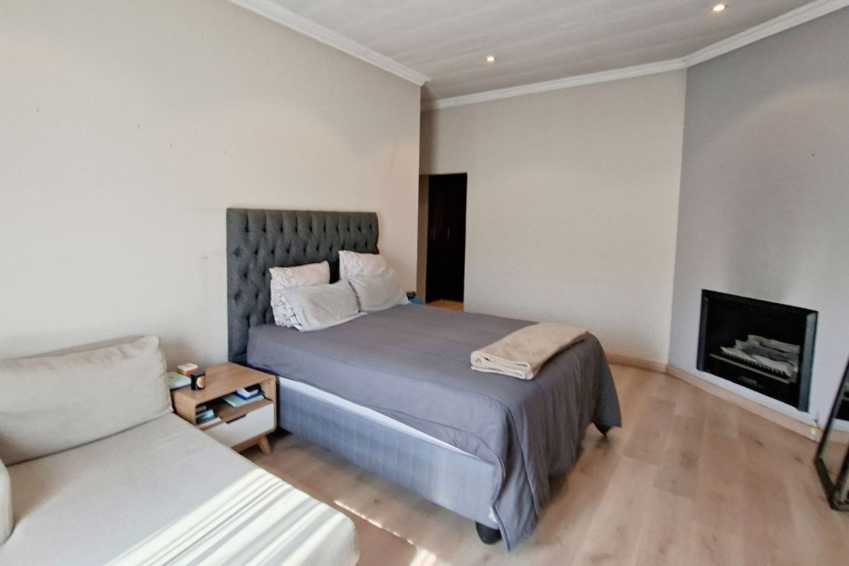 Spacious bedroom featuring light laminate flooring, neutral walls, cove ceiling molding, and a built-in fireplace.