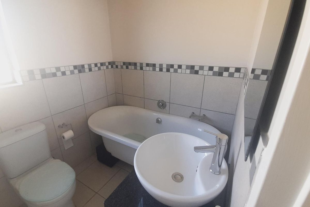 A compact bathroom featuring a white bathtub, a modern vessel sink on a vanity, and a standard toilet with tiled walls.