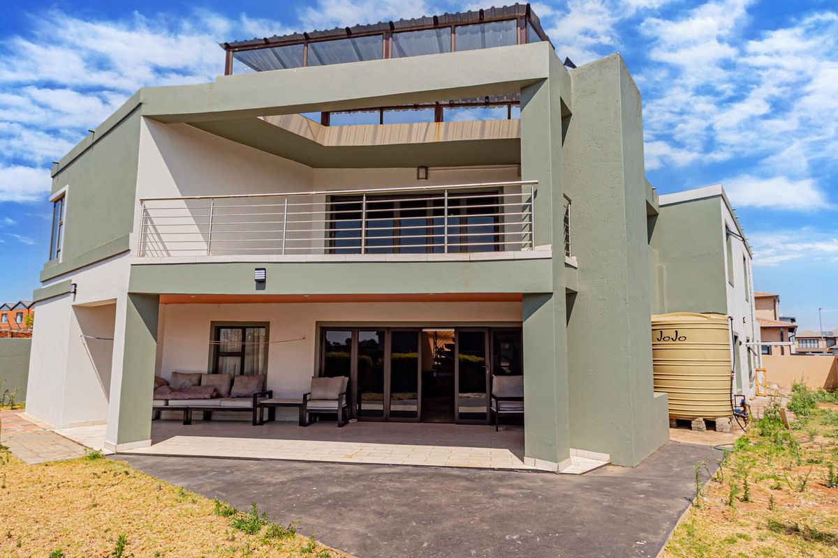 Rear view of a modern multi-story house featuring a covered patio, balcony, large glass sliding doors, and a water storage tank.