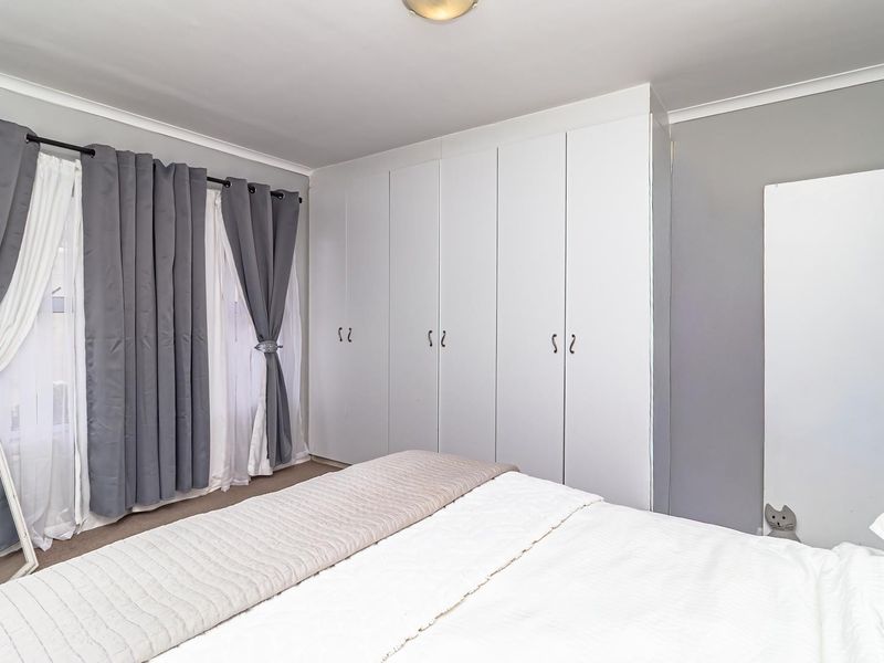 A well-maintained bedroom featuring neutral wall tones, fitted white built-in cupboards, and coving detail.