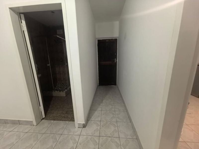 A clean, neutral hallway featuring tiled flooring and direct access to an adjacent bathroom with a shower enclosure.