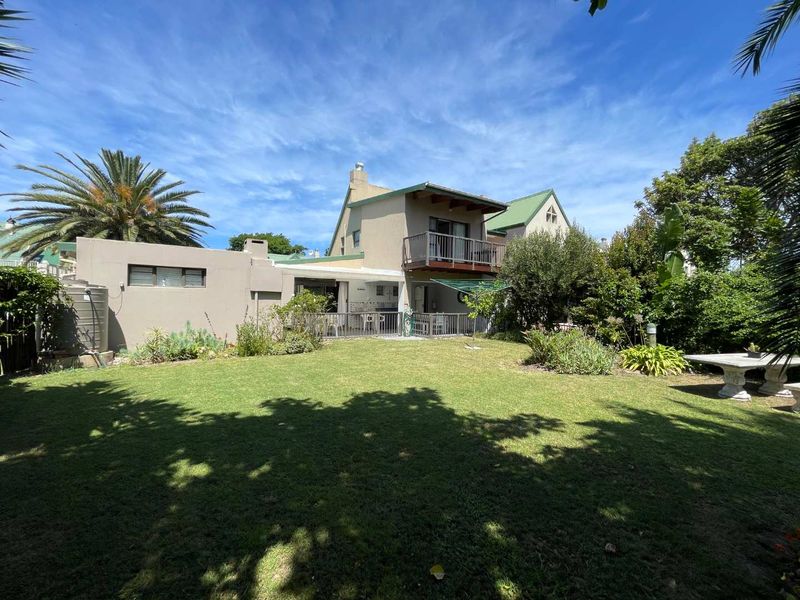 Rear view of the house featuring a spacious lawn, a ground-floor patio, and an upper-level balcony.