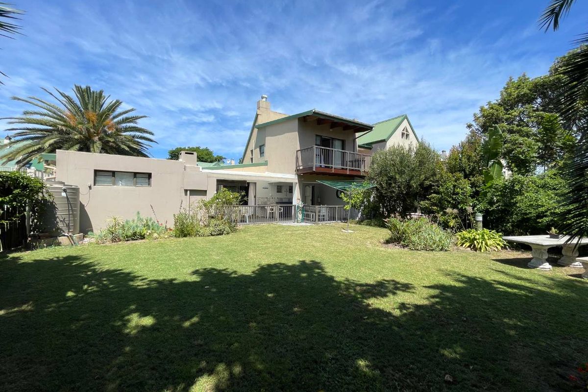 Rear view of the house featuring a spacious lawn, a ground-floor patio, and an upper-level balcony.
