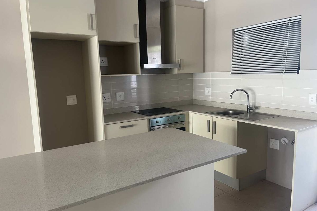 A functional kitchen featuring neutral cabinetry, stone-look countertops, a built-in oven with extractor fan, and a stainless steel sink.