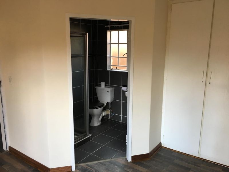 A compact bathroom featuring dark tiled walls and flooring, a shower enclosure, toilet, and basin, adjacent to a built-in cupboard area.
