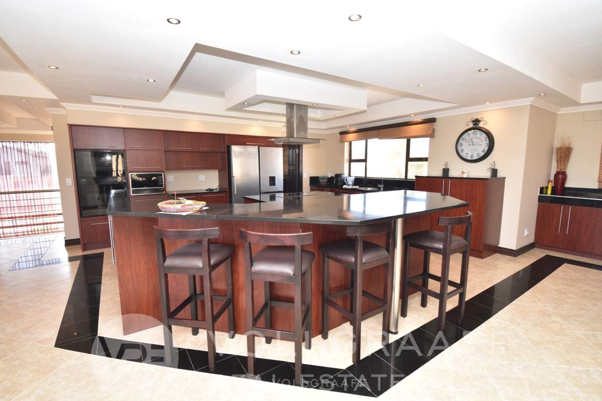 Spacious open-plan kitchen featuring dark wood cabinetry, granite countertops, a central island with breakfast bar seating, and a modern stainless steel extractor fan.