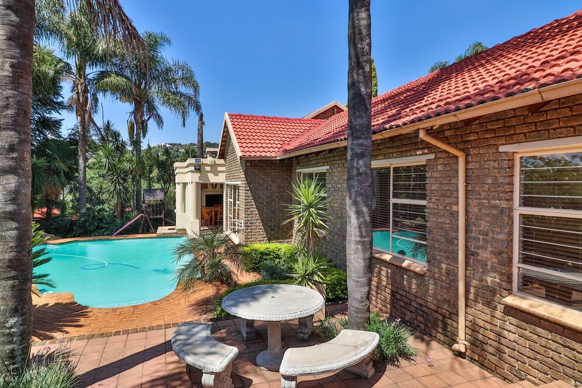 Rear exterior view featuring a swimming pool, brick facade, tiled roof, and a paved patio area surrounded by established garden landscaping.