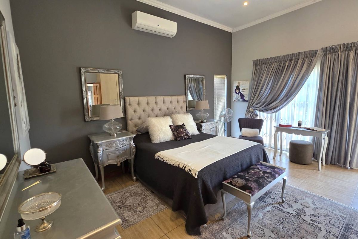 Spacious bedroom featuring tiled flooring, a wall-mounted air conditioning unit, and large windows with curtains providing natural light.