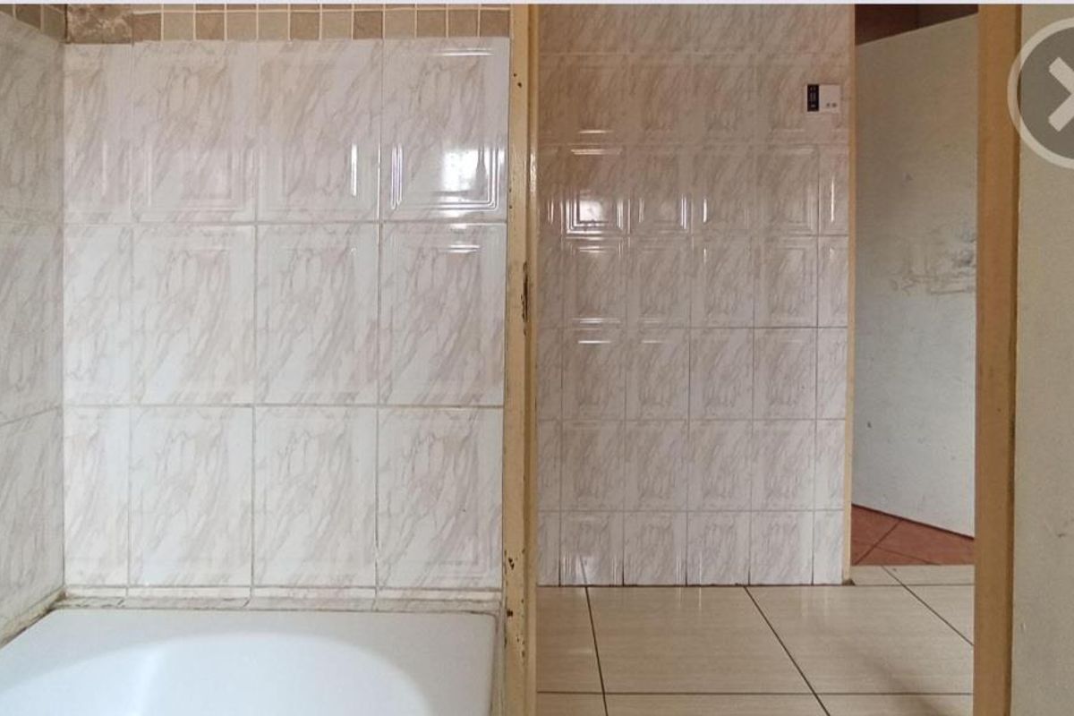 A dated bathroom featuring a built-in bathtub and ceramic tiling throughout, currently vacant and in need of cosmetic updates.