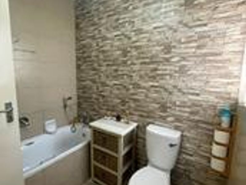 A functional bathroom featuring a bathtub, toilet, bidet, and a decorative stone-cladding feature wall.