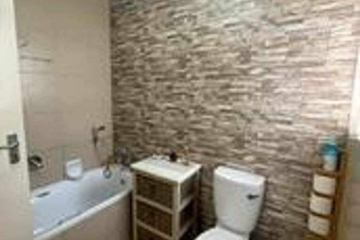 A functional bathroom featuring a bathtub, toilet, bidet, and a decorative stone-cladding feature wall.