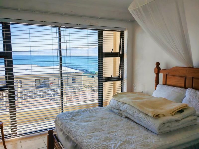 A bedroom featuring large windows with horizontal blinds, offering a clear view of the ocean and surrounding area, finished with tiled flooring.