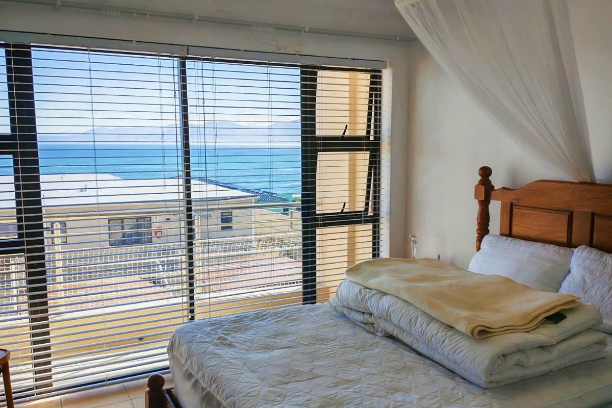 A bedroom featuring large windows with horizontal blinds, offering a clear view of the ocean and surrounding area, finished with tiled flooring.