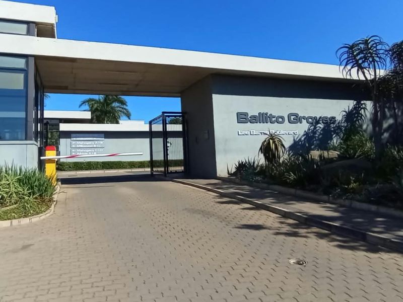 The entrance to Ballito Groves complex featuring a secure boom gate, guard house, and well-maintained landscaped gardens.