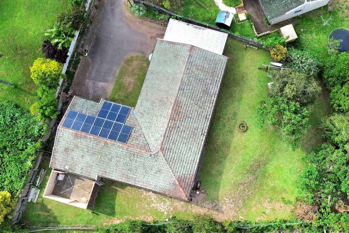 Aerial view of the property featuring a tiled roof with integrated solar panels, surrounding garden space, and driveway access.