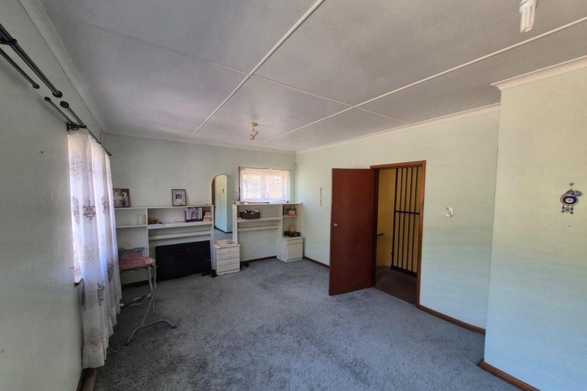 A bedroom featuring carpet flooring, built-in shelving, and a security gate at the doorway, offering a functional space ready for modernization.