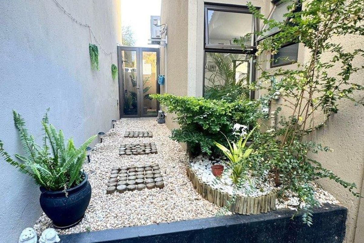 A narrow rear courtyard featuring a pebble garden, raised planter bed, and paved pathway leading to a glass door entrance.