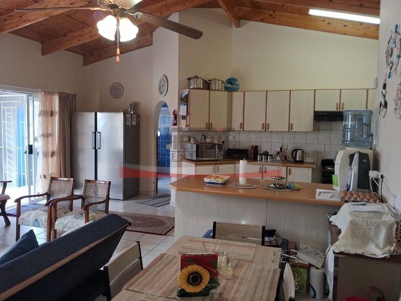Open-plan living and kitchen area featuring high exposed timber beam ceilings, a breakfast bar, and direct access to an outdoor patio area.