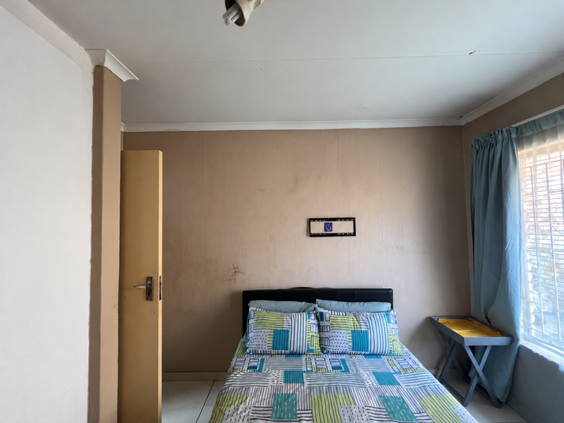 A bedroom featuring neutral wall tones, a window with security bars, and a built-in door, requiring minor cosmetic updates to improve its overall appeal.