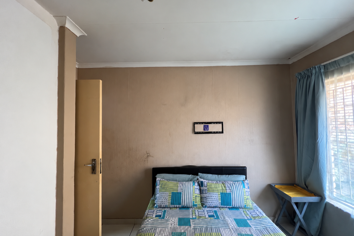 A bedroom featuring neutral wall tones, a window with security bars, and a built-in door, requiring minor cosmetic updates to improve its overall appeal.