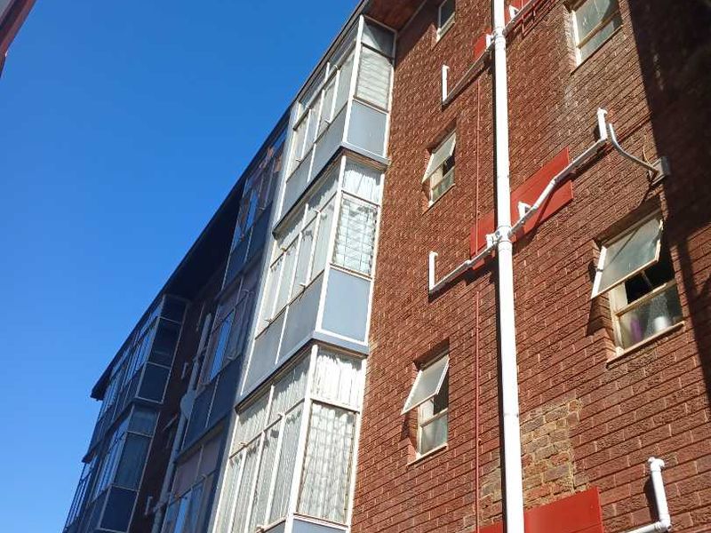 Low angle view of an apartment building exterior featuring red brick facade, enclosed balconies, and visible external plumbing infrastructure.