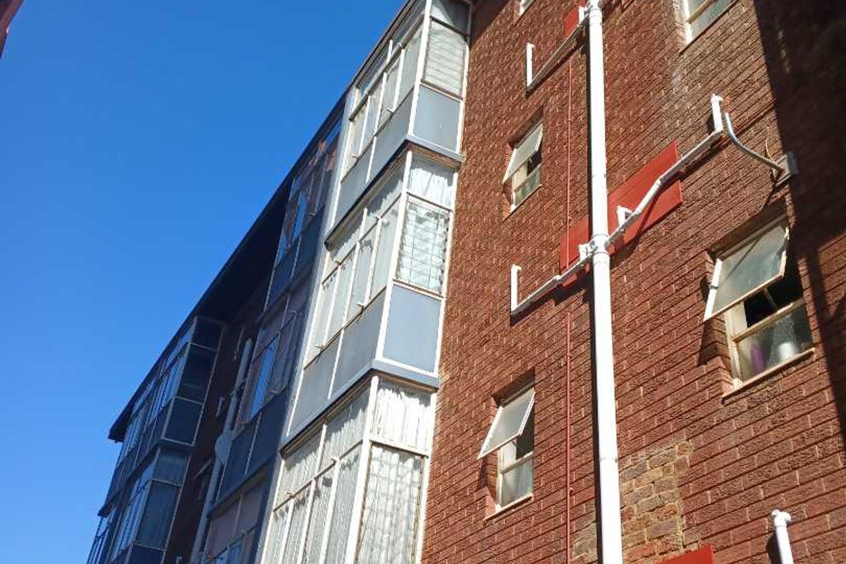 Low angle view of an apartment building exterior featuring red brick facade, enclosed balconies, and visible external plumbing infrastructure.