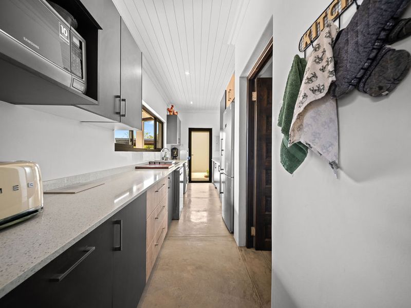 Modern scullery featuring sleek dark cabinetry, stone countertops, polished concrete floors, and a high-quality tongue and groove ceiling with recessed lighting.
