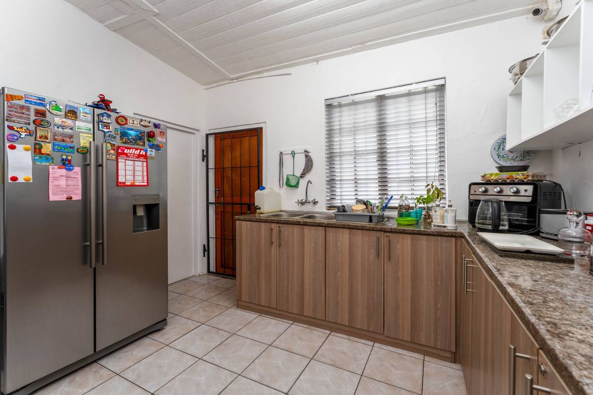 A functional kitchen featuring wood-look cabinetry, granite-style countertops, tiled flooring, and a security gate leading to an exterior entrance.