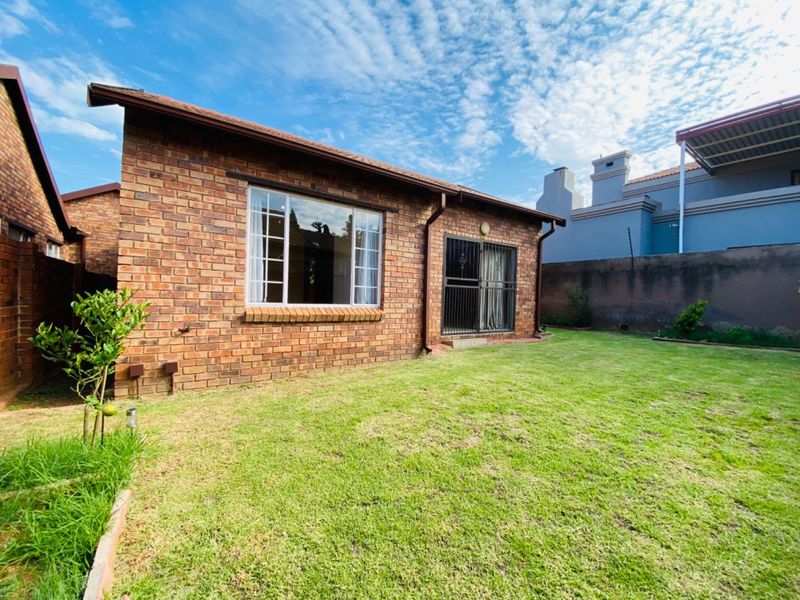 Rear view of the townhouse featuring a face brick facade, a well-maintained lawn, and a secure sliding door entrance.