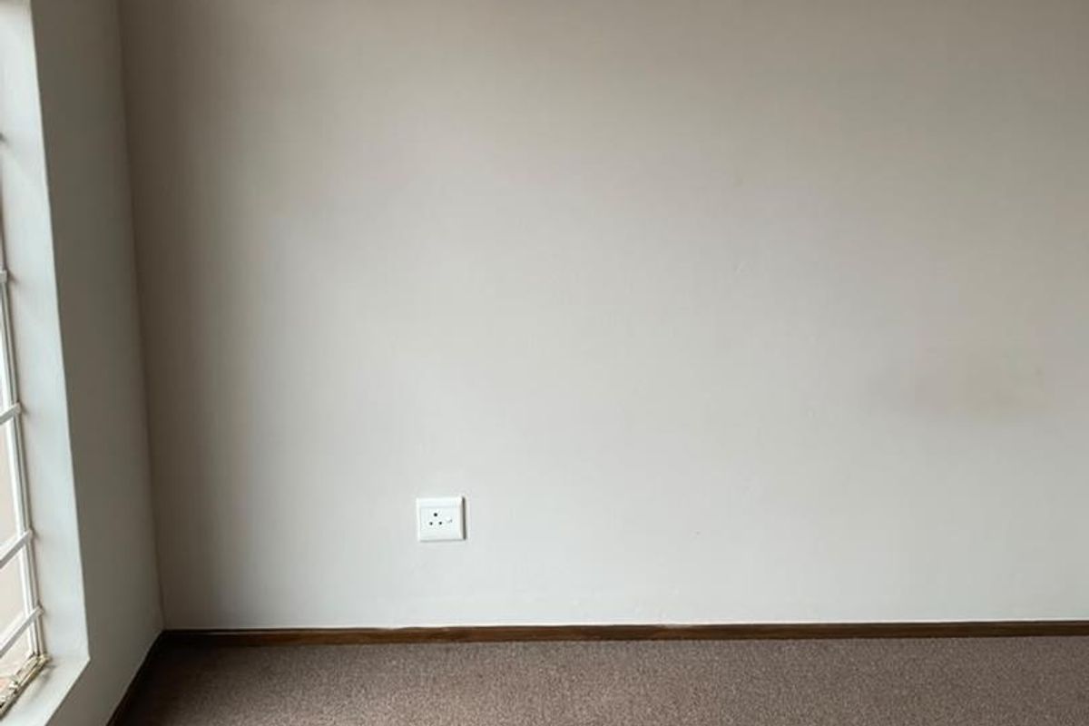 An empty bedroom featuring neutral walls, carpet flooring, and a large window, providing a blank canvas for personalization.