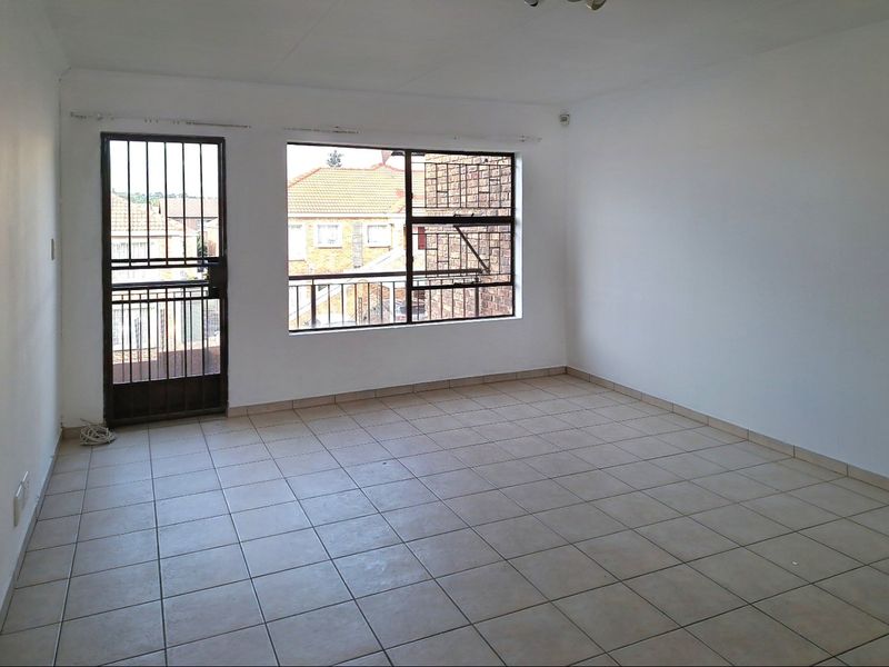 An empty, neutrally painted living area featuring tiled flooring, a security gate, and large windows with burglar bars.