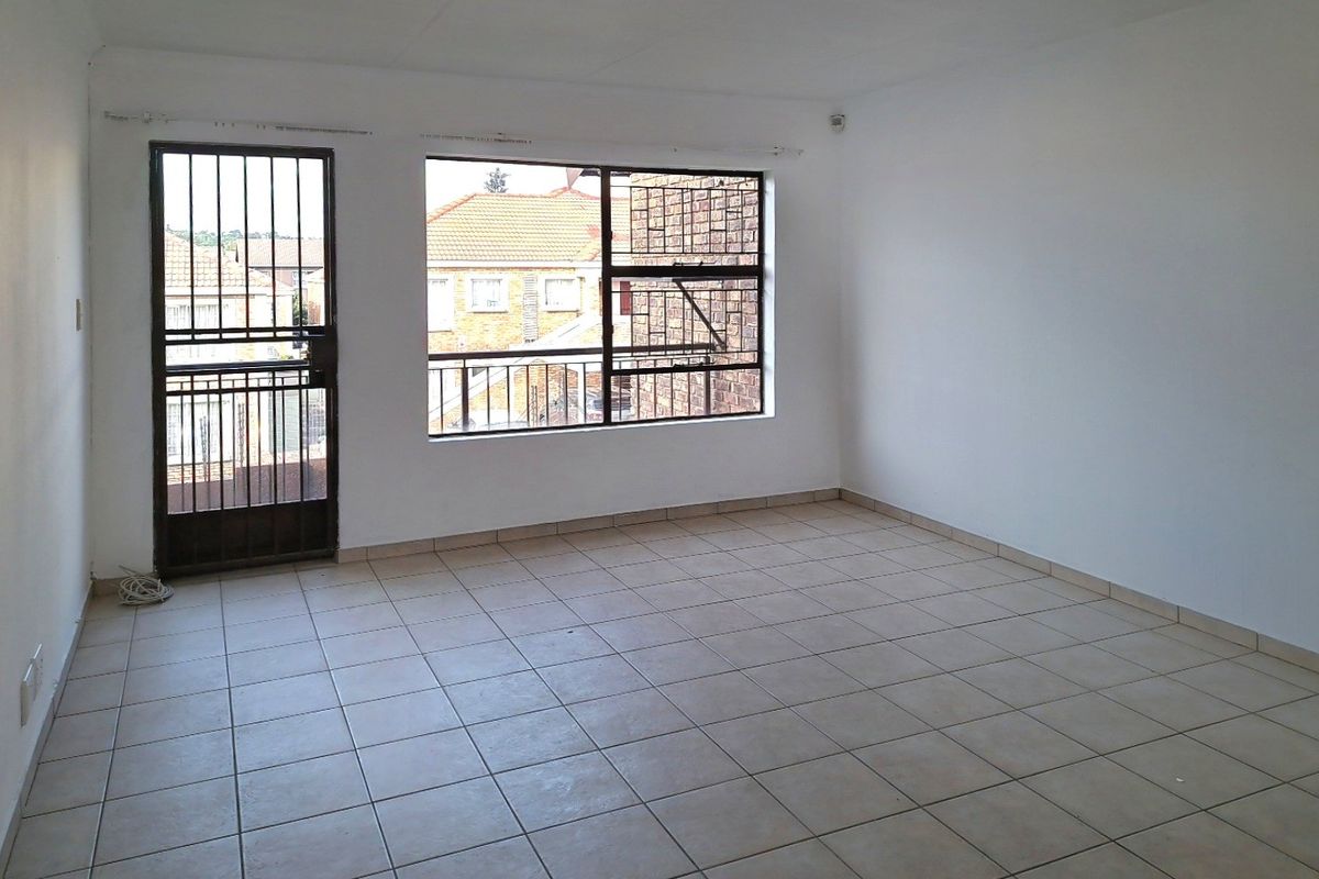 An empty, neutrally painted living area featuring tiled flooring, a security gate, and large windows with burglar bars.