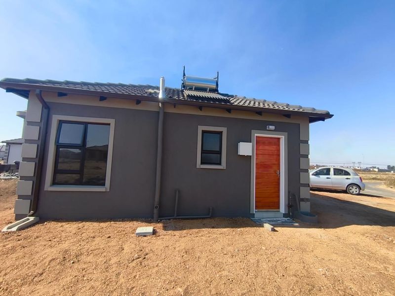 Rear view of a modern house featuring a tiled roof, solar water heating system, aluminium window frames, and a wooden entrance door.
