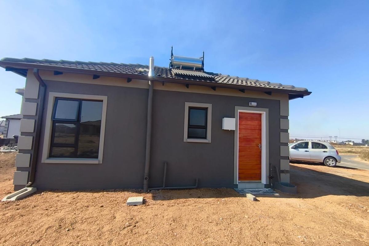 Rear view of a modern house featuring a tiled roof, solar water heating system, aluminium window frames, and a wooden entrance door.