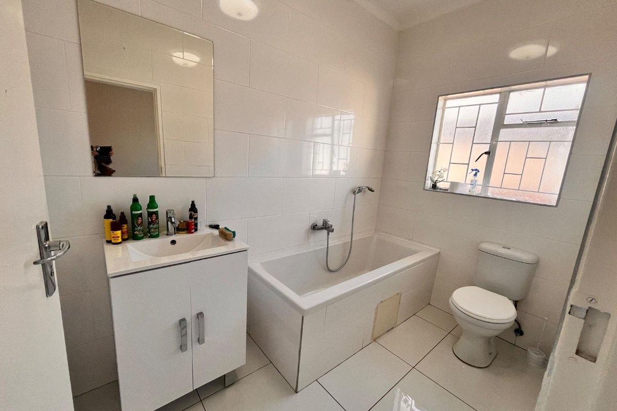 A functional bathroom featuring a white vanity, bathtub with shower mixer, toilet, and neutral wall and floor tiling.