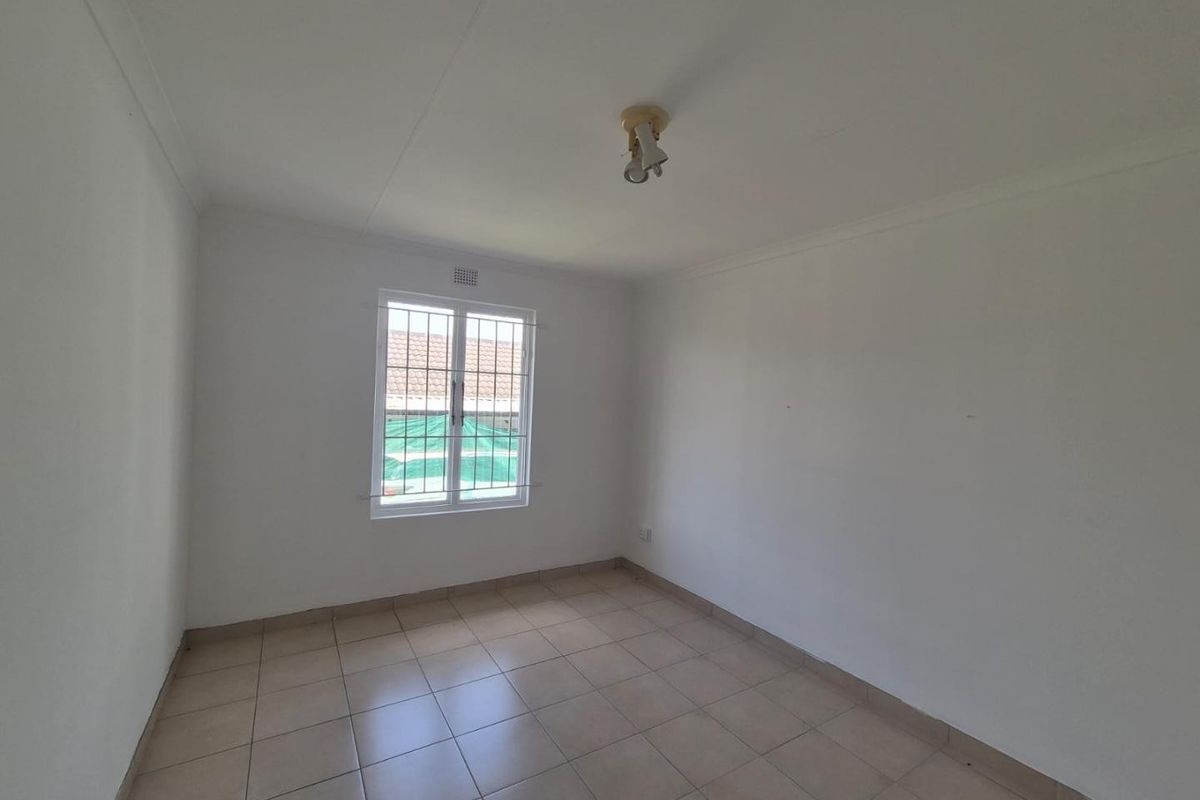 A clean, empty bedroom featuring neutral tiled flooring, white walls, and a window fitted with security bars.