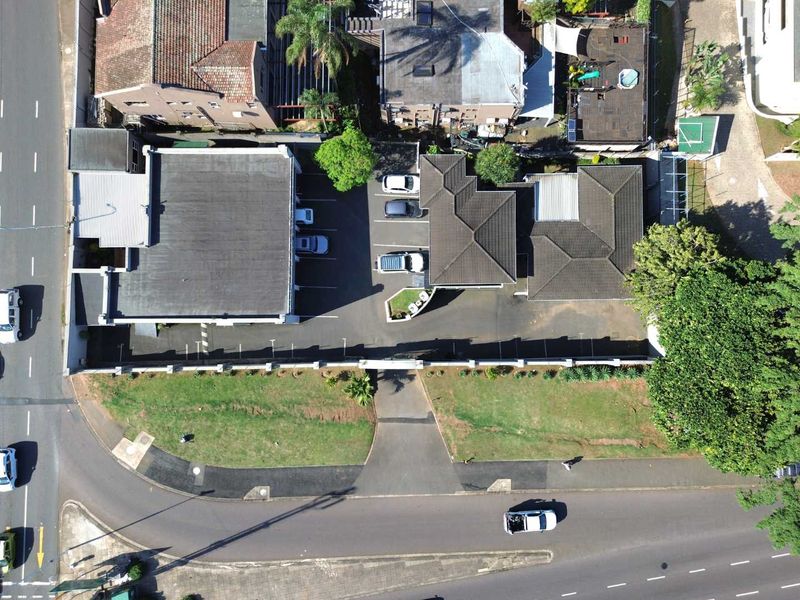 Aerial view of the commercial property featuring a paved parking area, multiple building structures with tiled roofs, and access from the main road.