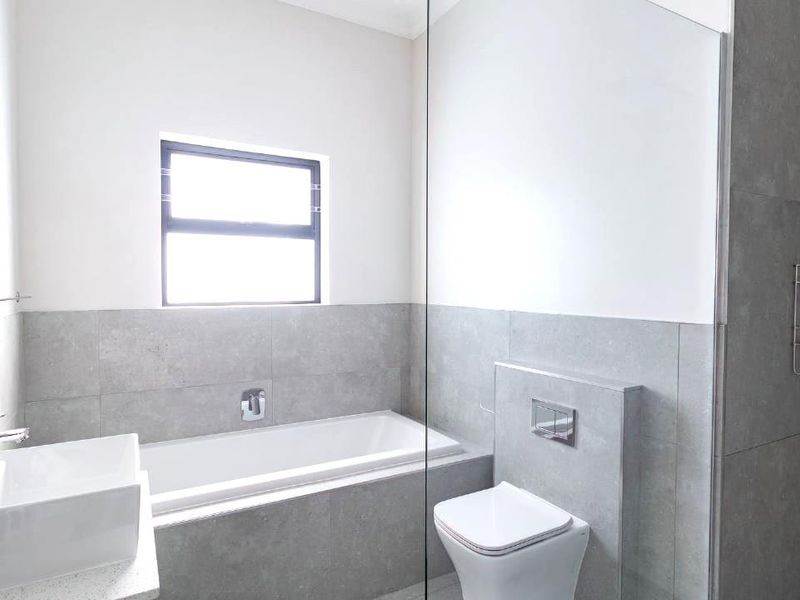 Modern bathroom featuring a built-in bathtub, wall-mounted toilet with concealed cistern, glass shower screen, and contemporary grey tiling.
