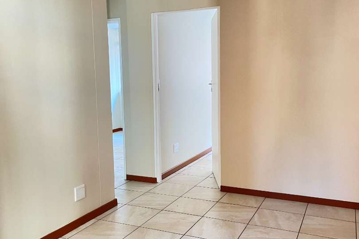 A clean, empty hallway featuring neutral wall paint and light-colored ceramic floor tiles, providing access to adjacent rooms.