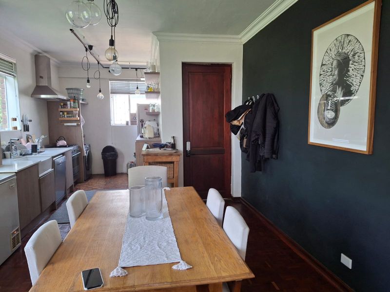 Open plan kitchen and dining area featuring parquet flooring, dark accent wall, and modern pendant lighting, creating a functional and connected living space.