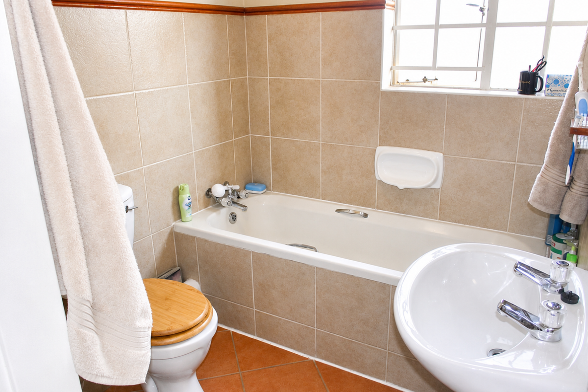 A functional bathroom featuring a bathtub, pedestal basin, and toilet, finished with neutral wall tiles and terracotta-style floor tiles.